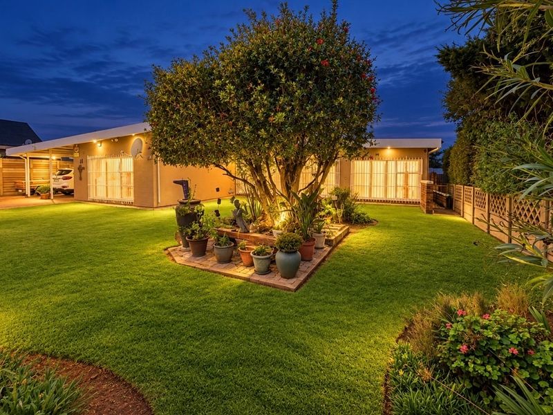 Well-maintained front exterior featuring a landscaped garden, mature tree, brick planter, and a convenient carport at dusk.