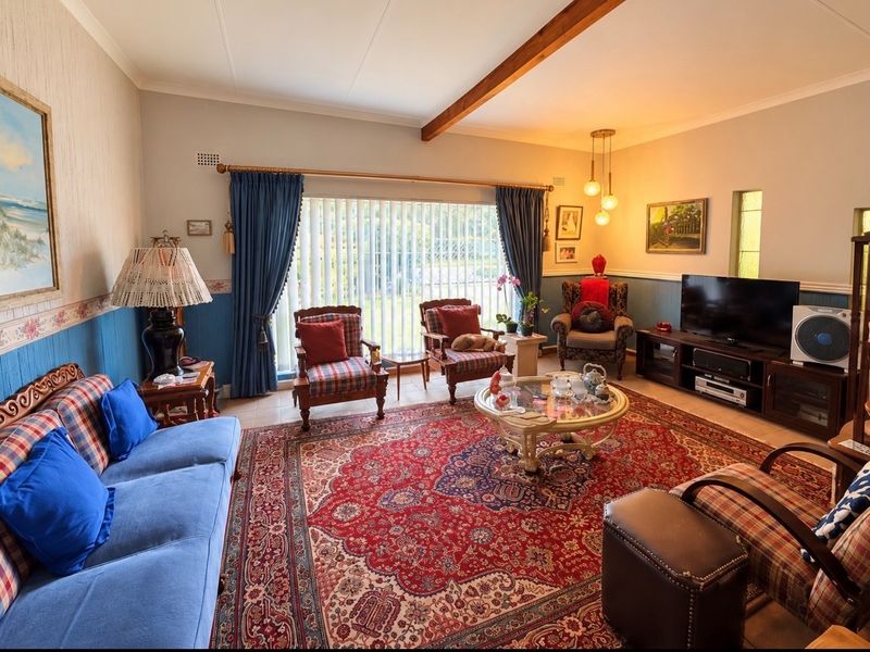 A comfortable living room featuring a decorative dado rail, exposed ceiling beam, and large windows with vertical blinds, offering a traditional aesthetic.