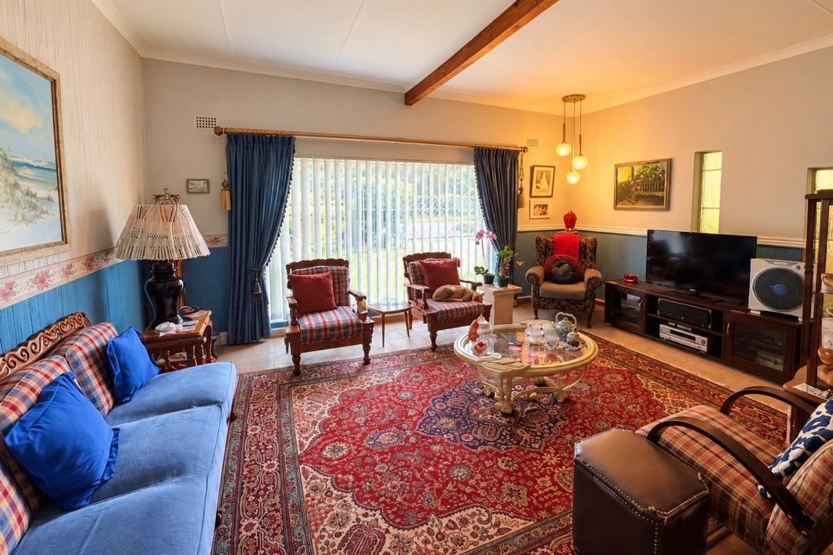 A comfortable living room featuring a decorative dado rail, exposed ceiling beam, and large windows with vertical blinds, offering a traditional aesthetic.