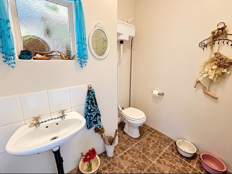 A functional bathroom featuring a wall-mounted basin, high-level cistern toilet, tiled splashback, and tiled flooring with an obscured glass window.