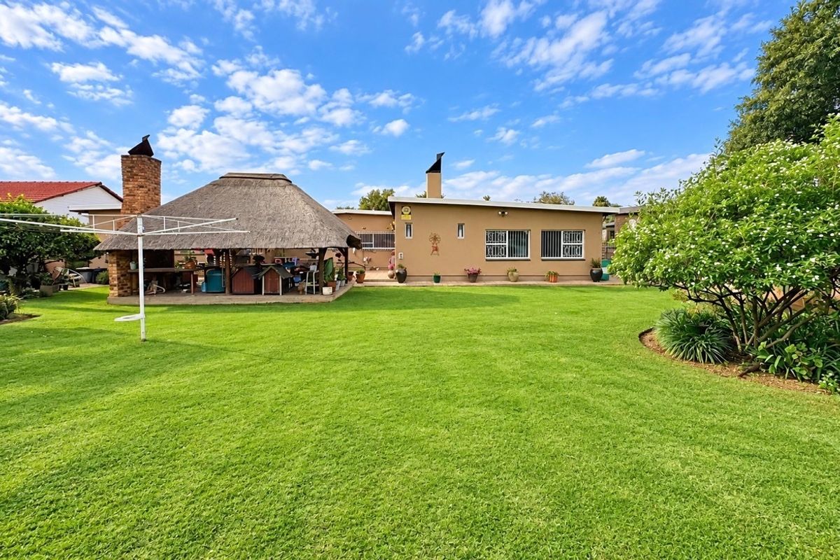 Spacious rear garden featuring a well-maintained lawn, a traditional thatched lapa with a built-in braai, and a solid brick exterior.
