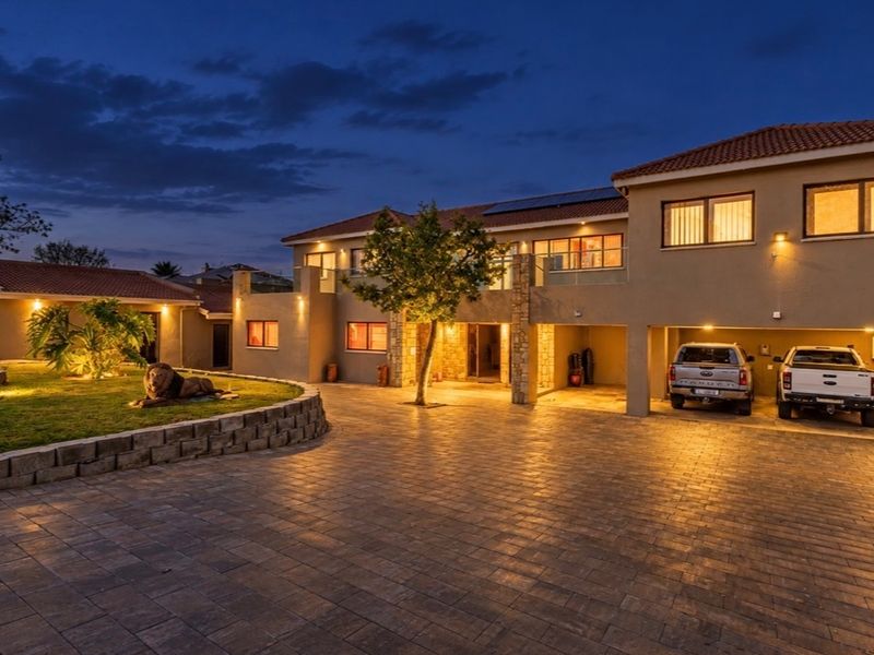A well-maintained double-story residence featuring a spacious paved driveway, integrated double garage, stone accents, and exterior lighting at dusk.
