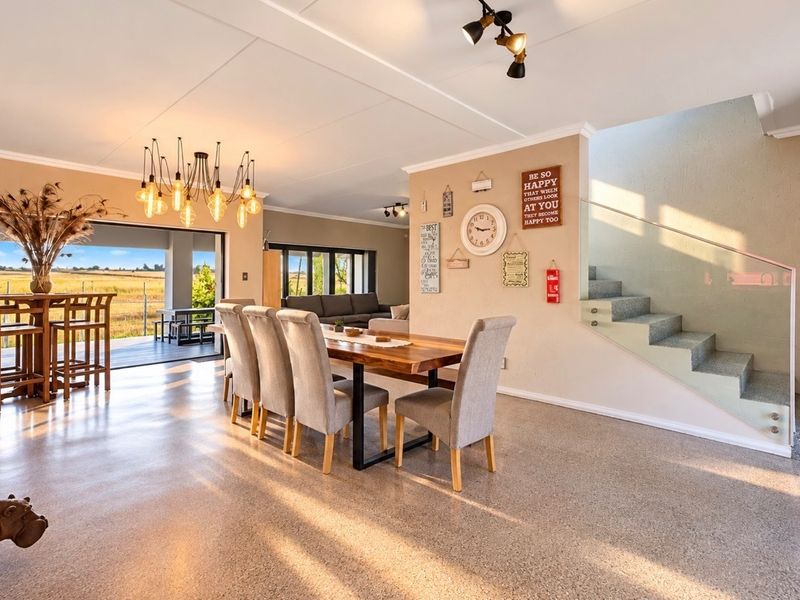 Spacious open-plan living and dining area featuring polished aggregate flooring, a modern staircase with glass balustrade, and seamless access to the outdoor patio.