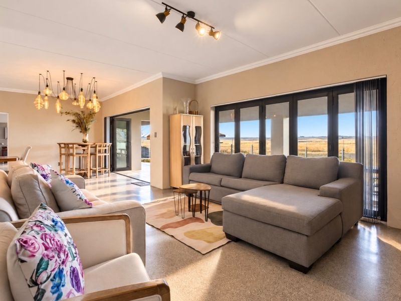 Spacious open-plan living area featuring polished concrete floors, modern track lighting, and large bi-fold doors opening to scenic outdoor views.