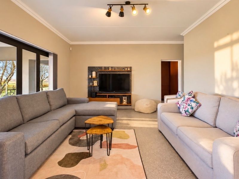 A well-lit living room featuring a built-in media unit, modern track lighting, and large sliding glass doors that provide access to the outdoor area.