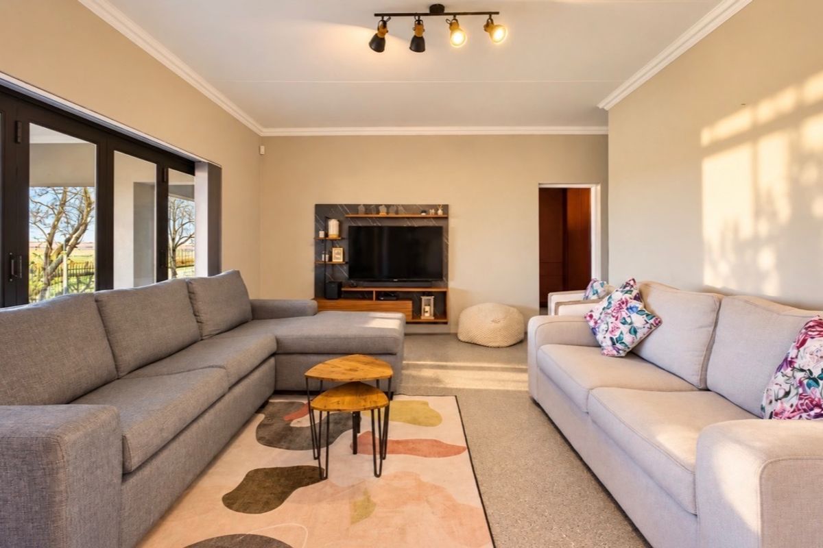 A well-lit living room featuring a built-in media unit, modern track lighting, and large sliding glass doors that provide access to the outdoor area.