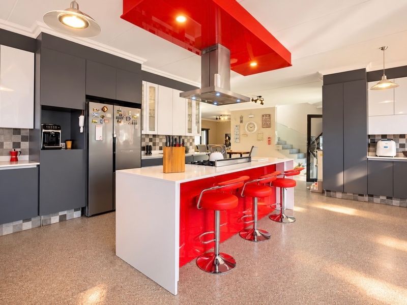 Modern kitchen featuring a large central island with breakfast bar, high-gloss cabinetry, stone countertops, and a prominent red bulkhead with integrated extractor fan.