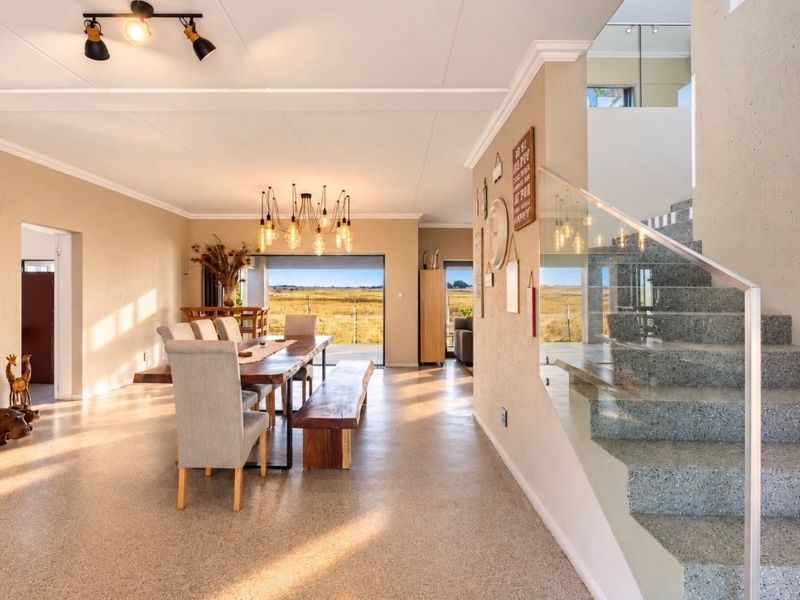 Spacious open-plan living and dining area featuring terrazzo stairs with glass balustrades, polished aggregate flooring, and large sliding doors opening to scenic views.