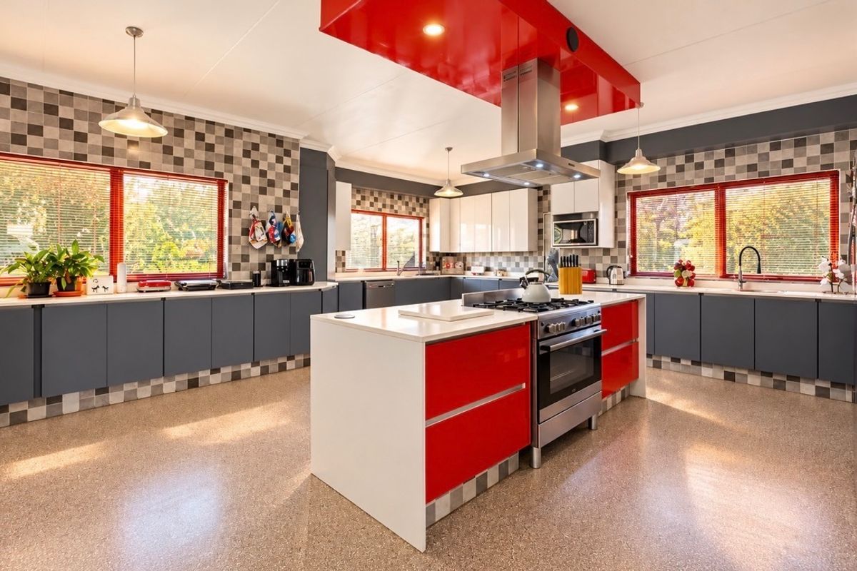 Spacious modern kitchen featuring a central island with gas cooktop, high-gloss cabinetry, stainless steel appliances, and extensive counter space with a tiled backsplash.