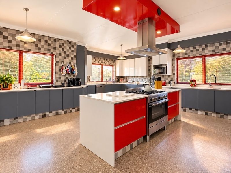 Spacious modern kitchen featuring a central island with gas cooktop, high-gloss cabinetry, stainless steel appliances, and extensive counter space with a tiled backsplash.
