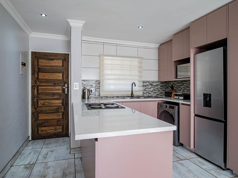 Modern kitchen featuring soft-toned cabinetry, stone countertops, a built-in hob, and tiled flooring, offering a functional and contemporary cooking space.