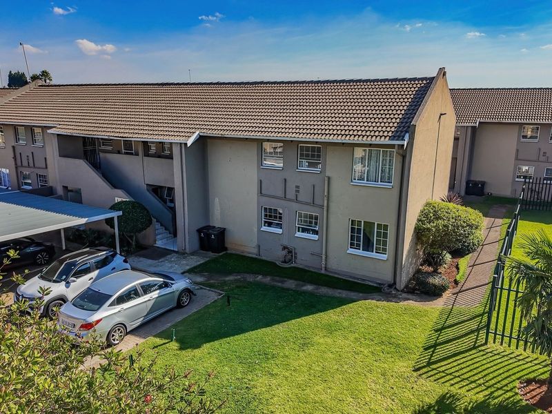 Aerial view of an apartment complex featuring a tiled roof, covered carport parking, and well-maintained communal garden areas.