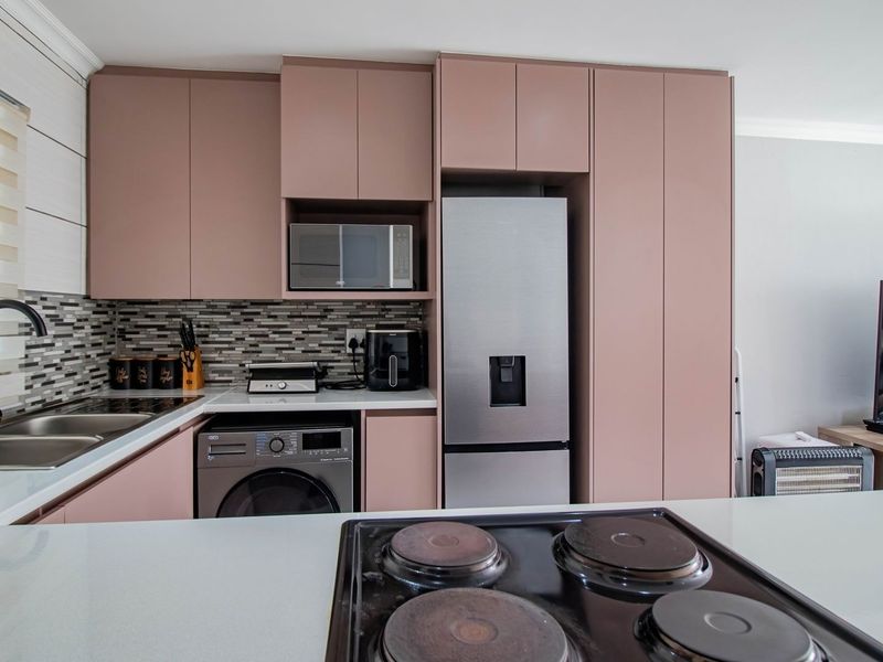 Modern kitchen featuring soft-toned cabinetry, stone countertops, mosaic backsplash, integrated appliances, and a functional layout with a central hob.