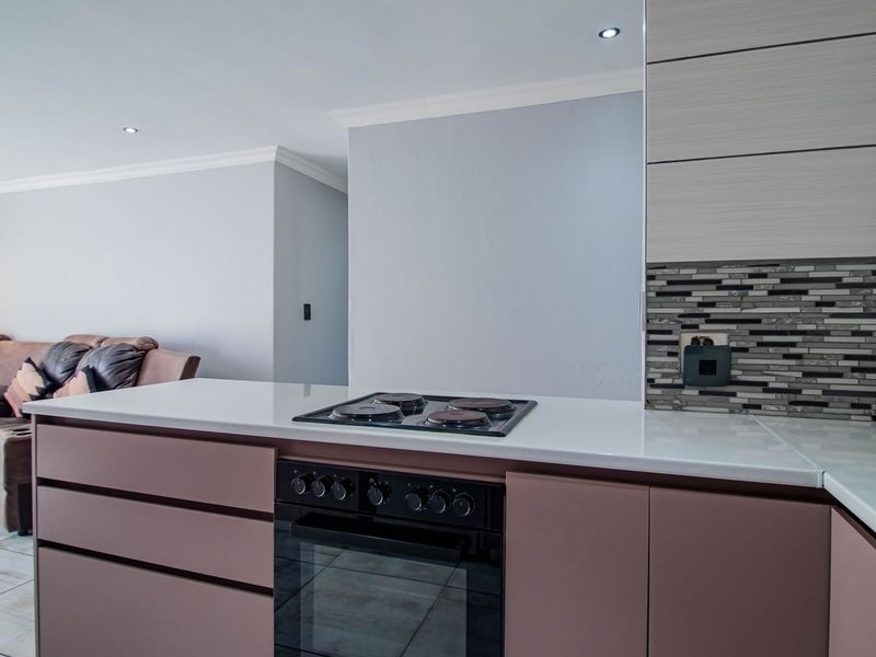 Modern open-plan kitchen featuring stone countertops, built-in oven, electric hob, and mosaic backsplash, seamlessly flowing into the adjacent living area.