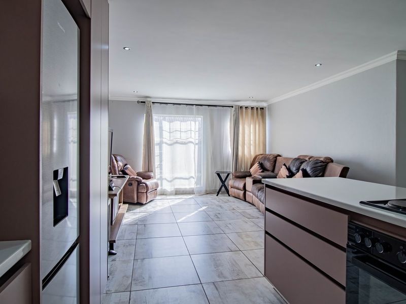 Modern open-plan living area featuring a sleek kitchen with built-in appliances, tiled flooring, and direct access to a balcony through sliding glass doors.
