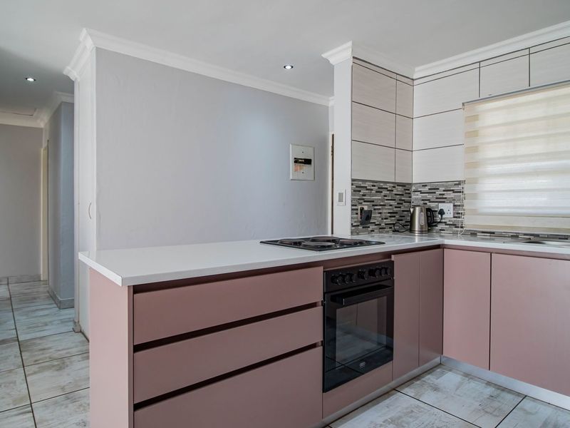 Modern kitchen featuring soft pink cabinetry, quartz countertops, a built-in oven with gas hob, and a stylish mosaic tile backsplash.