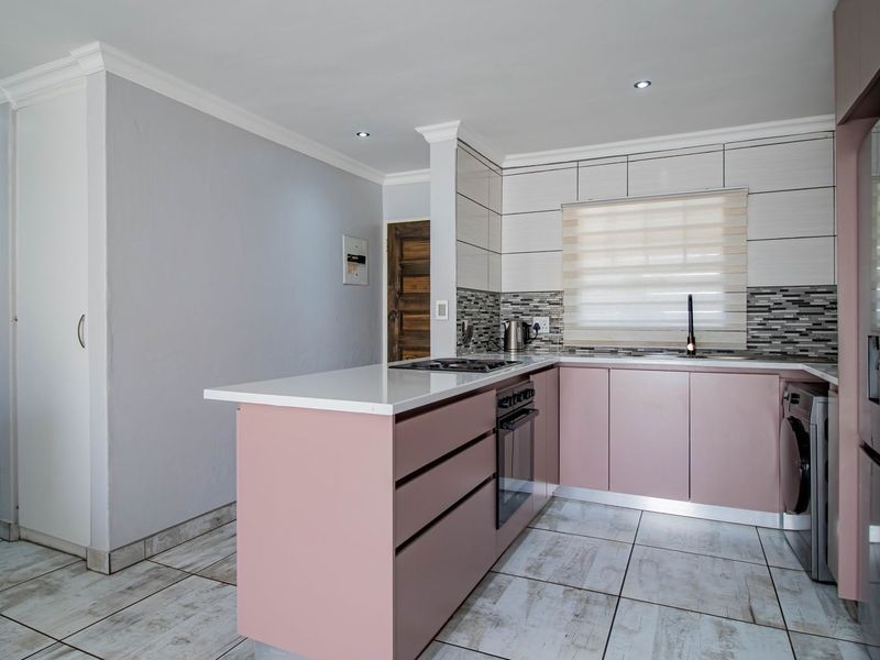 Modern kitchen featuring soft pink cabinetry, stone countertops, built-in oven, hob, and tiled flooring with integrated laundry space.
