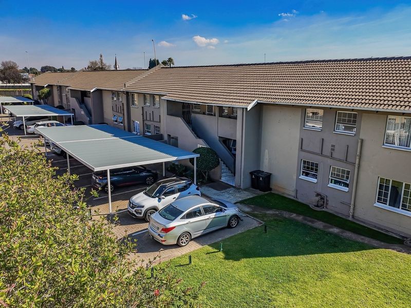 Aerial view of an apartment complex featuring a tiled roof, covered parking carports, and well-maintained communal garden areas.