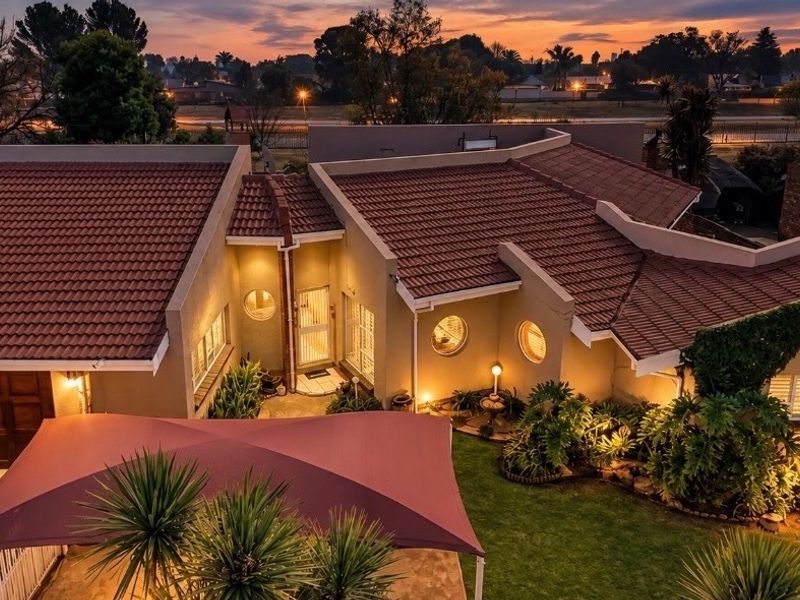 Aerial view of a residential property at dusk, featuring a tiled roof, paved driveway, garage, and a shaded outdoor patio area.