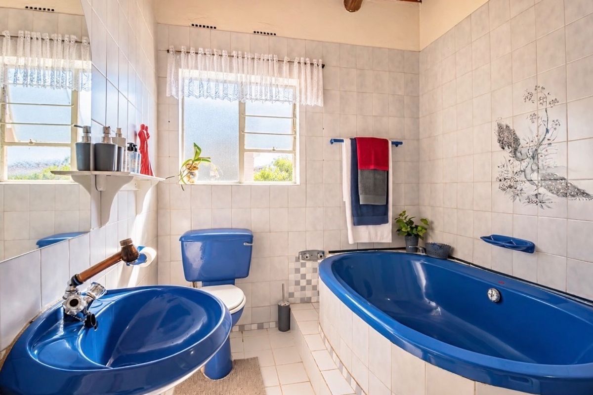 A dated bathroom featuring blue sanitaryware, including a bathtub and pedestal basin, with white wall tiles and a window for natural light.