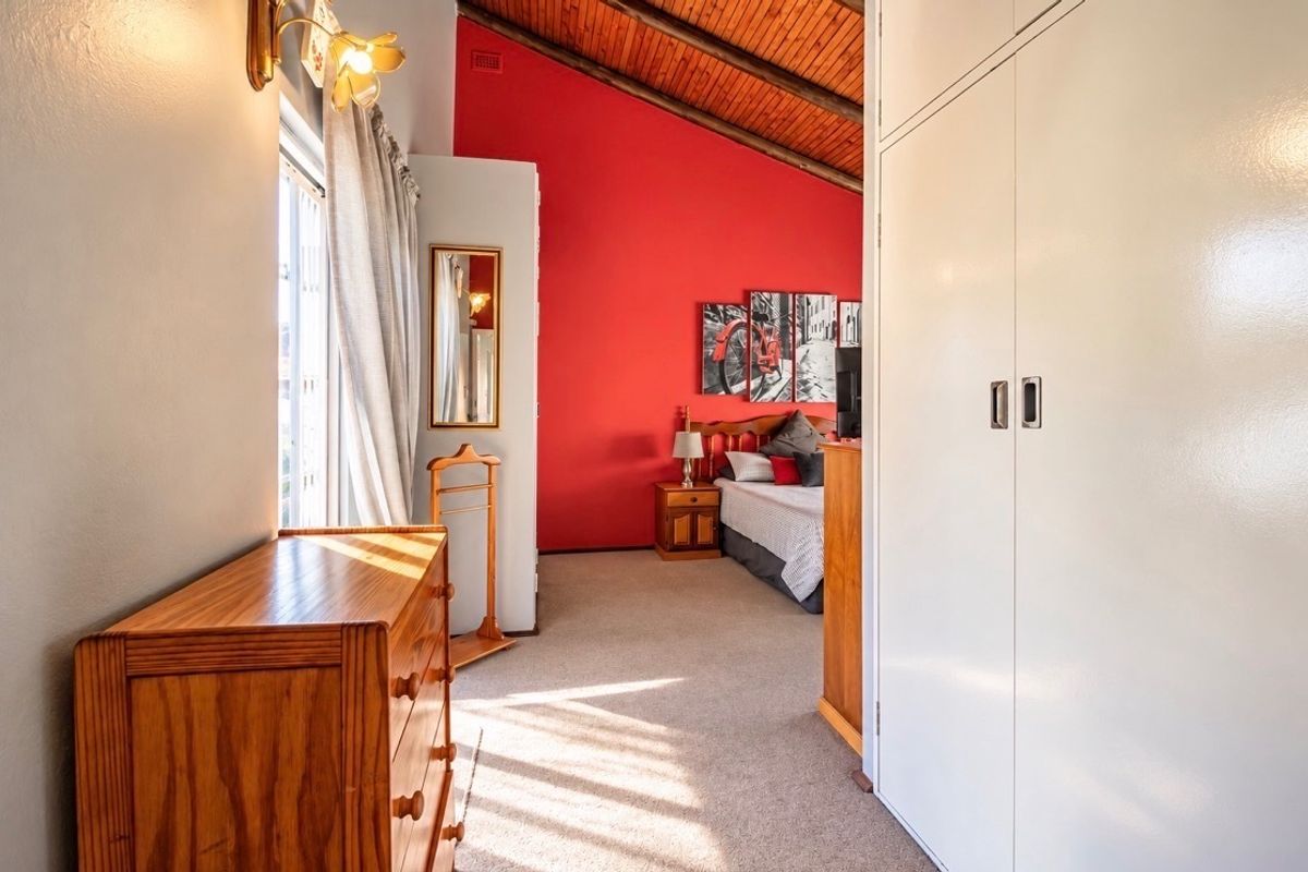 A bedroom featuring a vaulted timber ceiling, carpeted flooring, and built-in cupboards, offering a spacious layout with natural light.