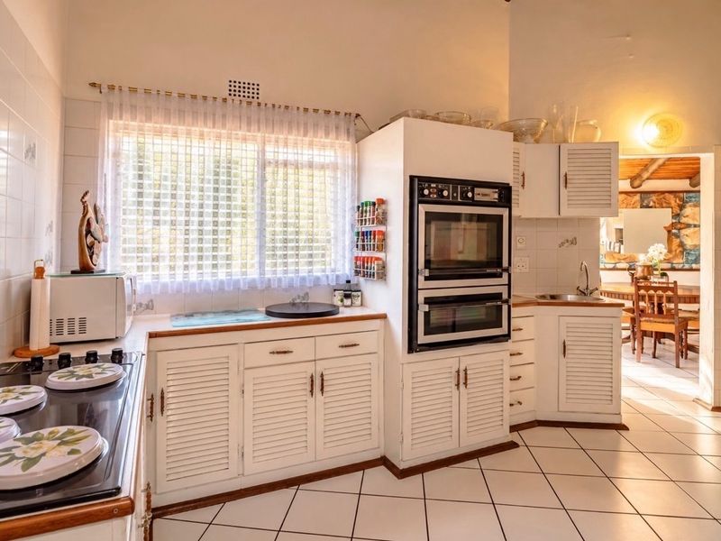 A functional kitchen featuring white louvered cabinetry, a built-in double oven, hob, and tiled flooring, offering a classic layout with potential for modern updates.