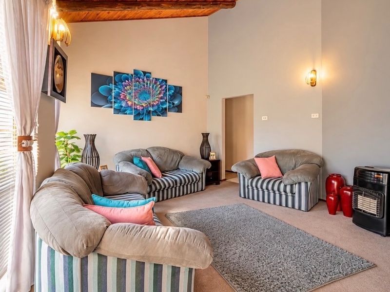 Spacious living room featuring exposed timber ceiling beams, wall sconce lighting, and a built-in gas heater, creating a warm and inviting atmosphere.
