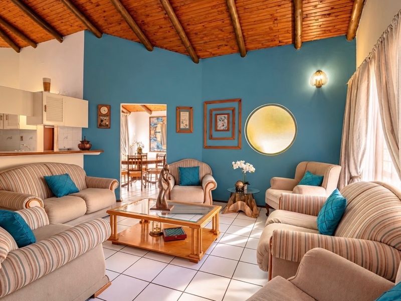 Open plan living area featuring a vaulted timber beam ceiling, ceramic tiled flooring, and a circular feature window, with an adjoining kitchen and dining space.