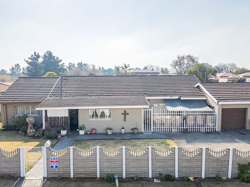Front elevation of a single-story residential house featuring a tiled roof, paved driveway, garage, and secure precast boundary wall.