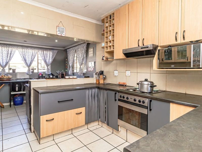 A functional kitchen featuring built-in cabinetry, laminate countertops, and integrated appliances, with tiled flooring and backsplash throughout the workspace.