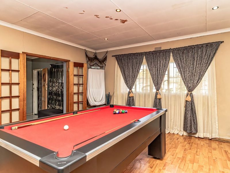 A living area featuring laminate flooring, timber-framed glass doors, and security bars on windows. The ceiling shows visible signs of water damage.