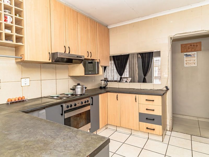 Functional kitchen featuring light wood cabinetry, dark laminate countertops, built-in oven and hob, and tiled splashbacks with a convenient pass-through window.