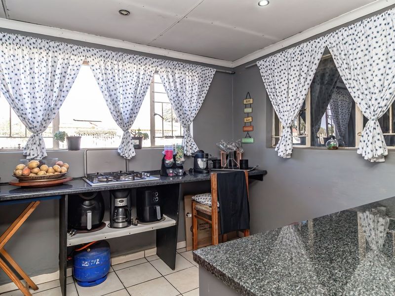 A functional kitchen area featuring granite countertops, a built-in gas hob, and tiled flooring, currently requiring updates to cabinetry and finishes.