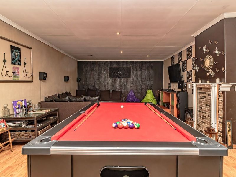 A dedicated entertainment room featuring a brick fireplace, recessed ceiling lighting, and laminate flooring, currently set up as a games and media space.