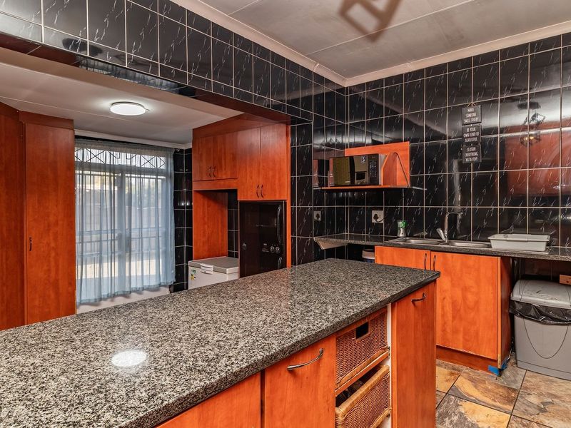 Functional kitchen featuring granite countertops, wooden cabinetry, and dark tiled walls, offering a practical layout with ample storage and workspace.
