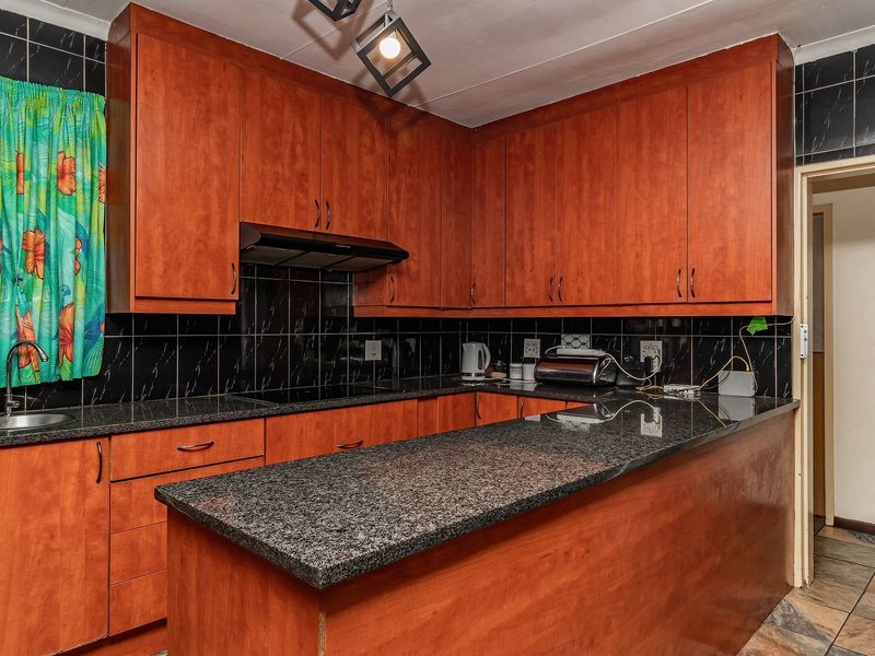 A functional kitchen featuring wood-finish cabinetry, granite countertops, a tiled backsplash, and an integrated extractor fan.