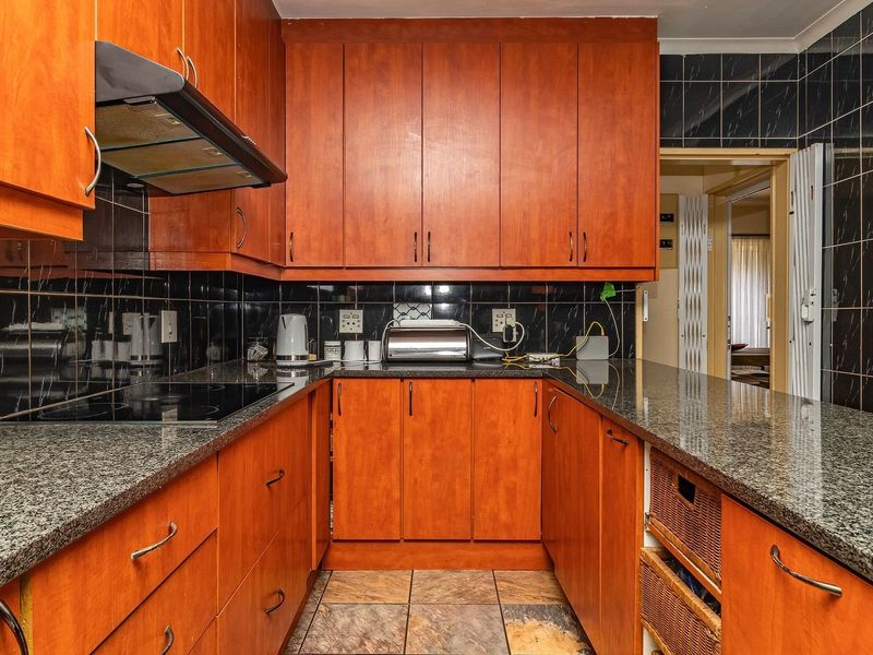 A functional kitchen featuring granite countertops, wooden cabinetry, an electric hob with extractor fan, and dark tiled backsplash.