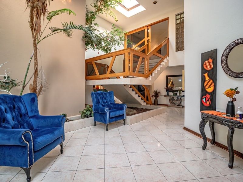 Spacious double-volume entrance hall featuring a prominent wooden staircase, tiled flooring, and a large skylight that provides ample natural light.