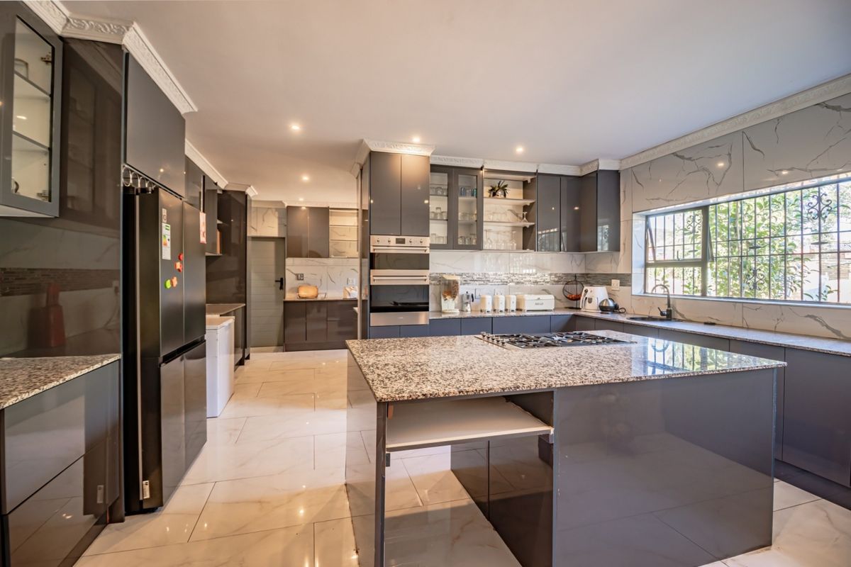 Modern kitchen featuring high-gloss cabinetry, granite countertops, a central island with a gas hob, built-in appliances, and elegant marble-look wall tiling.