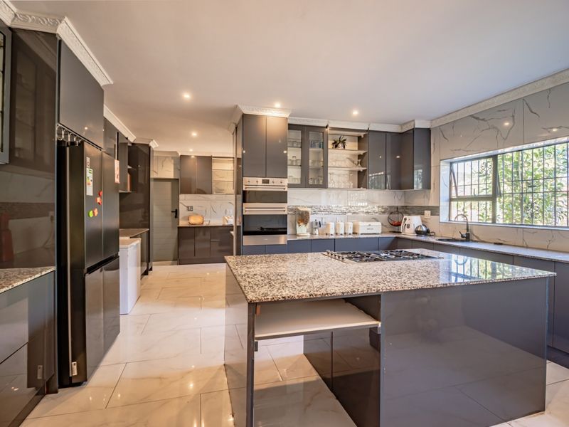 Modern kitchen featuring high-gloss cabinetry, granite countertops, a central island with a gas hob, built-in appliances, and elegant marble-look wall tiling.