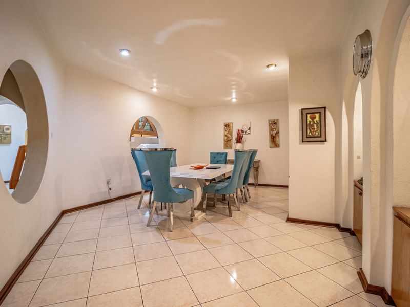 A spacious dining room featuring ceramic floor tiles, recessed lighting, and unique arched wall openings that provide architectural character to the space.