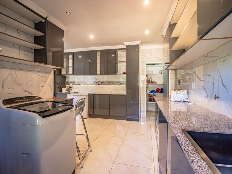 Modern scullery featuring high-gloss cabinetry, granite countertops, marble-look wall tiling, and a dedicated pantry area with ample storage space.
