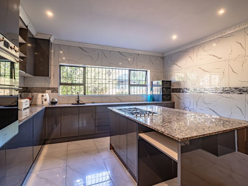 Modern kitchen featuring high-gloss cabinetry, granite-topped island with integrated gas hob, built-in oven, and elegant marble-look wall tiling.