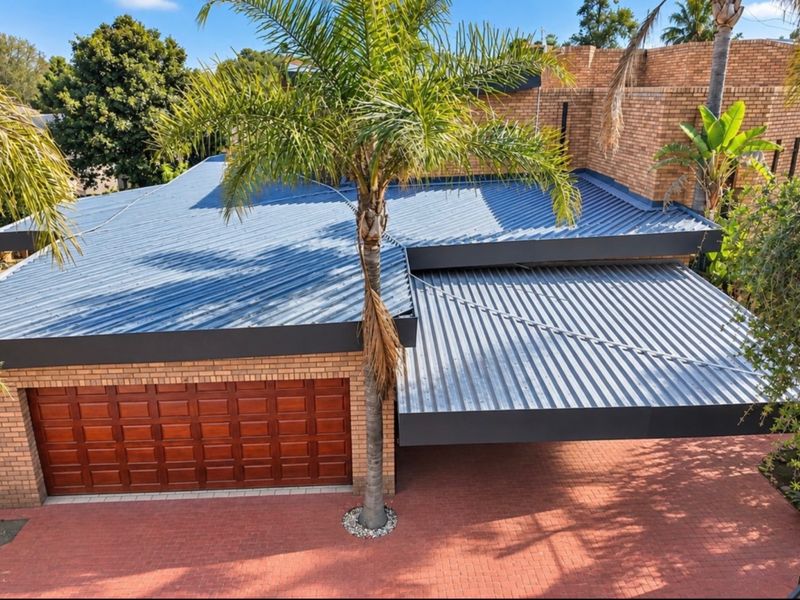 Elevated view of the property front featuring a brick facade, corrugated metal roofing, a paved driveway, and a covered carport area.