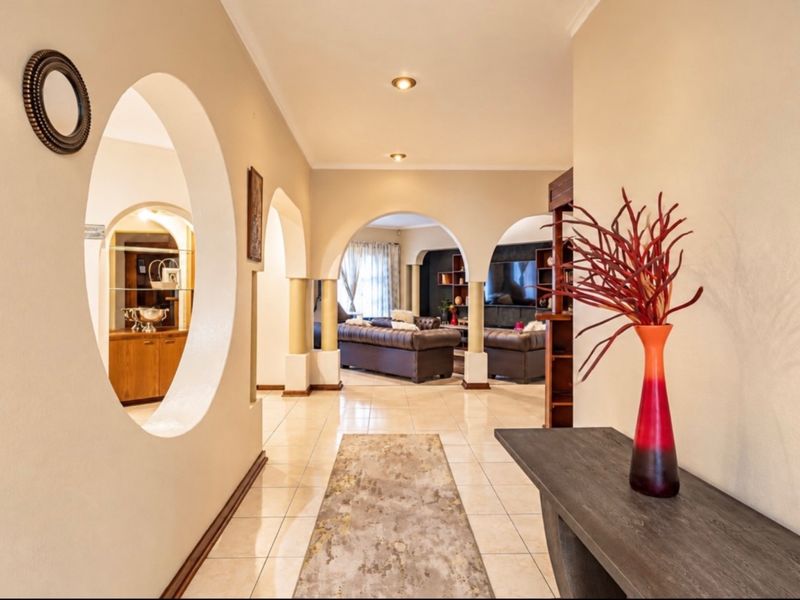A spacious, well-lit hallway featuring elegant arched doorways, tiled flooring, and a unique circular architectural cutout connecting to adjacent living spaces.