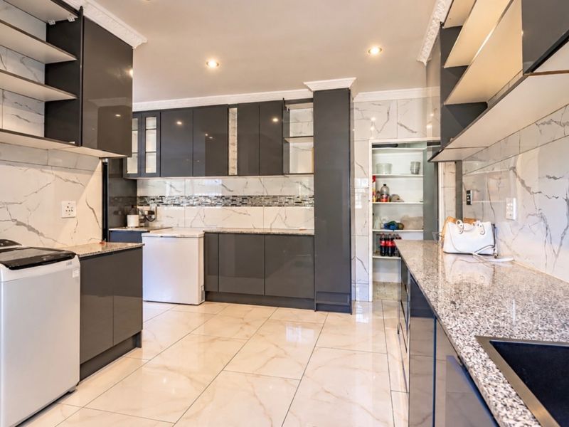 Modern kitchen featuring high-gloss cabinetry, granite countertops, marble-look wall tiles, and a convenient walk-in pantry with ample storage space.