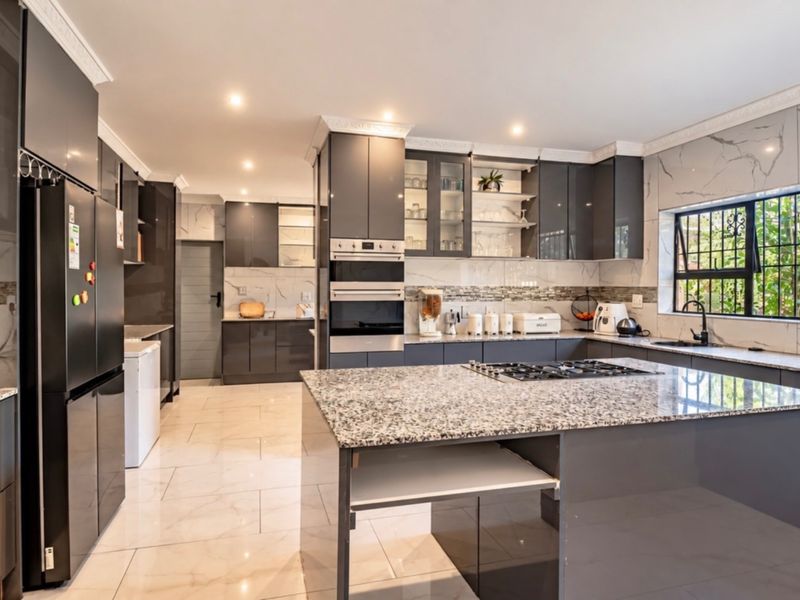 Modern kitchen featuring high-gloss cabinetry, granite countertops, a central island with a gas hob, and integrated appliances with marble-effect wall tiling.