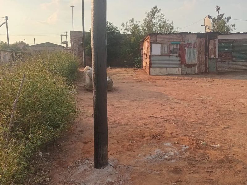 A vacant residential plot featuring a utility pole and a small, weathered corrugated metal structure on unpaved ground.