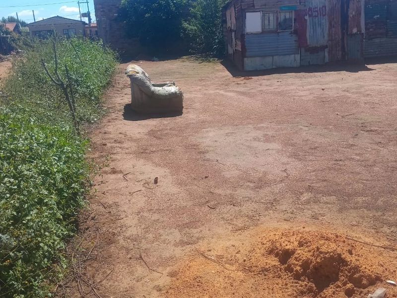 A view of a vacant residential plot featuring an existing corrugated metal structure and unpaved ground.