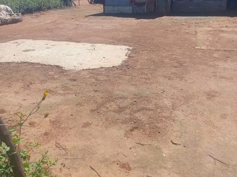 A vacant residential plot featuring a concrete slab foundation and an existing corrugated metal structure in a state of significant disrepair.